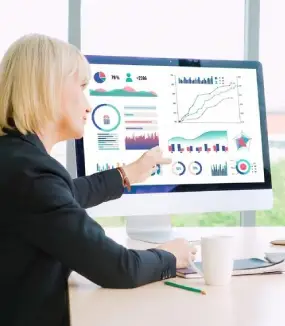 A woman points at a computer monitor that displays a complex, colorful dashboard of business charts and statistics