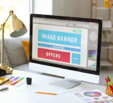 A modern desktop computer setup showing a website design interface on the monitor with large text elements like "IMAGE BANNER" and "OFFERS," suggesting on-page optimization